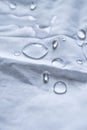 Crystal pure water droplets on a white fabric drapery with folds shining in light