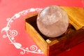 Crystal quartz ball in wooden box on decorated red background