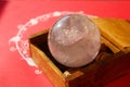 Crystal quartz ball in wooden box on decorated red background