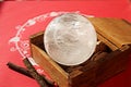 Crystal quartz ball in wooden box on decorated red background