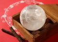 Crystal quartz ball in wooden box on decorated red background