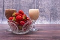 Crystal vase with ripe red strawberries and two glasses of cocktails stand on wooden table. Royalty Free Stock Photo
