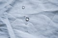 Crystal water droplets shining in light on white fabric drapery with folds