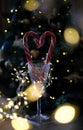 crystal wine glass with red striped heart-shaped lollipops against of glowing garlands and bokeh of a festive tree Royalty Free Stock Photo