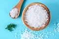 Crystals of large sea salt in a wooden bowl and spoon and dill on a blue table. Background for advertising salt. Table salty. Salt Royalty Free Stock Photo