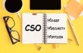 CSO - Chief Security Officer. Text on notepad and office accessories on yellow desk