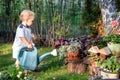 Cuate adorable caucasian blond little toddler boy in watering flowerbed flower pot with green plastic can outdoors. Fun baby boy