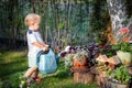 Cuate adorable caucasian blond little toddler boy in watering flowerbed flower pot with green plastic can outdoors. Fun baby boy Royalty Free Stock Photo