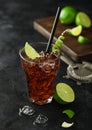 Cuba Libre cocktail in heavy crystal glass with ice and lime slice and peel, with straw and fresh limes with bar strainer on black Royalty Free Stock Photo