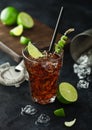 Cuba Libre cocktail in heavy crystal glass with ice and lime slice and peel, with straw and fresh limes with bar strainer on black Royalty Free Stock Photo