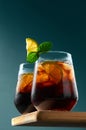 Cuba Libre or Long Island Cocktail with rum, cola and lime in glasses on wooden board on dark blue background. Royalty Free Stock Photo