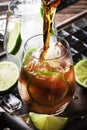 Cuba libre preparation alcohol cocktail with golden rum, lemon juice, cola, lime and ice, dark bar counter background, bar tools, Royalty Free Stock Photo