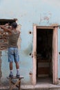 Cuban bricklayer working on old rundown pastel colored dwelling