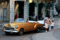 Cuban man driving a large golden classic car in busy Havana street