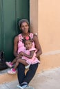 Cuban mother with cute little toddler girl resting in front of frontdoor.