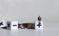 Cube arithmetic operator and a pile of coins. A miniature man sitting on a mathematical symbol cube.