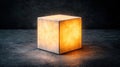 A cube-shaped lamp with a glowing orange light inside sits on a dark gray surface. Royalty Free Stock Photo