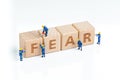 Cube wooden block with alphabets combine the word FEAR with miniature people men help building on white background using as greed