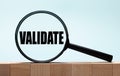 Cubes on a light blue wooden background. On them a magnifying glass with the word VALIDATE