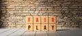 Cubes with the message FAIR PLAY in front of a brick wall on wooden floor