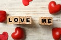 Cubes with phrase Love Me and red hearts on white table, flat lay