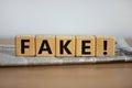 Cubes placed on a newspaper form the word `fake`. Beautiful wooden table. White background. Business concept. Copy space Royalty Free Stock Photo