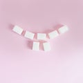Cubes of white sugar are laid out in the form of a smile with teeth on a pink background