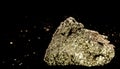 Cubic pyrite crystal stone, cat gold, in front of a black background with blurred fragments at a distance.