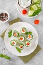 Cucumbers rolls with cream cheese, salted salmon and fresh herbs served on a white plate on a concrete background. Selective focus Royalty Free Stock Photo