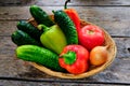 Cucumbers, tomatoes, sweet bell peppers and onions in a basket on a wooden table in a rustic style Royalty Free Stock Photo