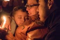 Mother holds sleeping child and candle for Festival de Luzes Fe