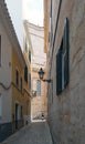 A woman walking past the end of a long quiet alley in cuitadella menorca with old historic buildings and the steps of the old cath