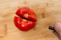 Cutting fresh red tomato with knife with sharp blade into two halves on a wooden kitchen board Royalty Free Stock Photo