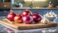 A selection of fresh vegetable: red onion and garlic, sitting on a chopping board against blurred kitchen background copy space