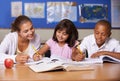 Cultivating the authors of tomorrow. A young teacher sitting with her two ethnic pupils while they study.