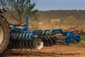 Cultivator on ground road by ploughed field against village