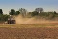 Cultivator operates on ploughed field raises dust in spring