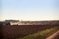 cultivator raises dust on ploughed field near ground road