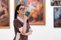 Cultural education and excursion. Portrait of caucasian pretty young woman wearing glasses contemplates arts. Defocused Royalty Free Stock Photo