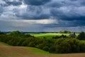 Dark cumulonimbus clouds with sun light spot over green autumn field. Royalty Free Stock Photo