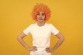 cunning funny girl with fancy look wearing orange hair wig on yellow background, emotions