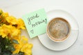 Cup of aromatic coffee, yellow freesias and Good Morning note on white marble table, flat lay Royalty Free Stock Photo