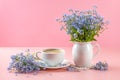 Cup of aromatic coffee and a bouquet of forget-me-nots on a pink background