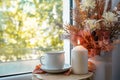 Cup of autumn tea and yellow dry leaves in the vase, candle near a window. Hot drink for autumn Royalty Free Stock Photo