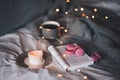 Cup of blac tea with scented burning candle with open paper book and pink fruit macaroons in bed on knit jumper over glow lights a Royalty Free Stock Photo