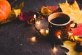 Cup of black coffee, autumn maple leaves and lights on dark background. Cozy autumn seasonal background.