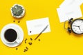 Cup of black coffee, coffee beans, black alarm clock, pens, white paper cards on yellow background Flat lay top view copy space. Royalty Free Stock Photo