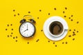 Cup of black coffee, coffee beans, black alarm clock on yellow background Flat lay top view copy space. Minimalistic food concept Royalty Free Stock Photo