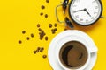 Cup of black coffee, coffee beans, black alarm clock on yellow background Flat lay top view copy space. Minimalistic food concept Royalty Free Stock Photo