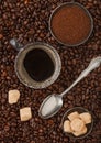 Cup of black coffee with ground coffee and cane sugar with silver spoon inside fresh coffee beans background Royalty Free Stock Photo